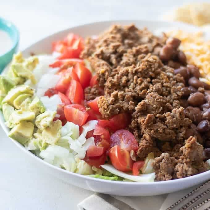 Taco Salad in white bowl with avocado, onion, tomatoes and ground beef.