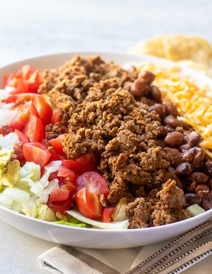 White Bowl with layered ground beef, tomatoes, cheese, and beans all on lettuce