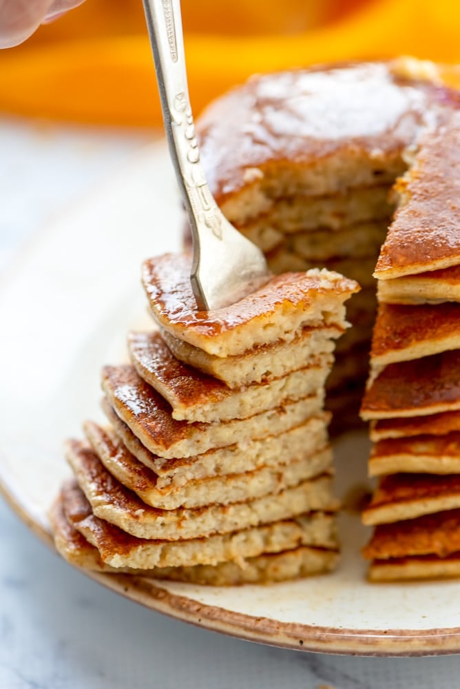 Stack of banana oatmeal pancakes on plate showing triangle bite out of stack. 