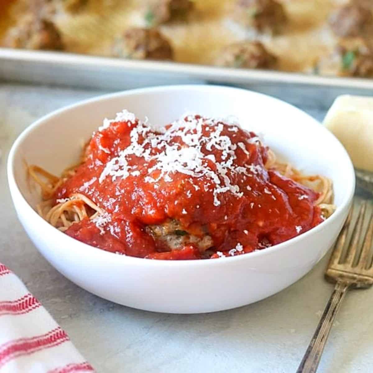 Bowls of homemade spaghetti meatballs next to baking tray with baked meatballs.