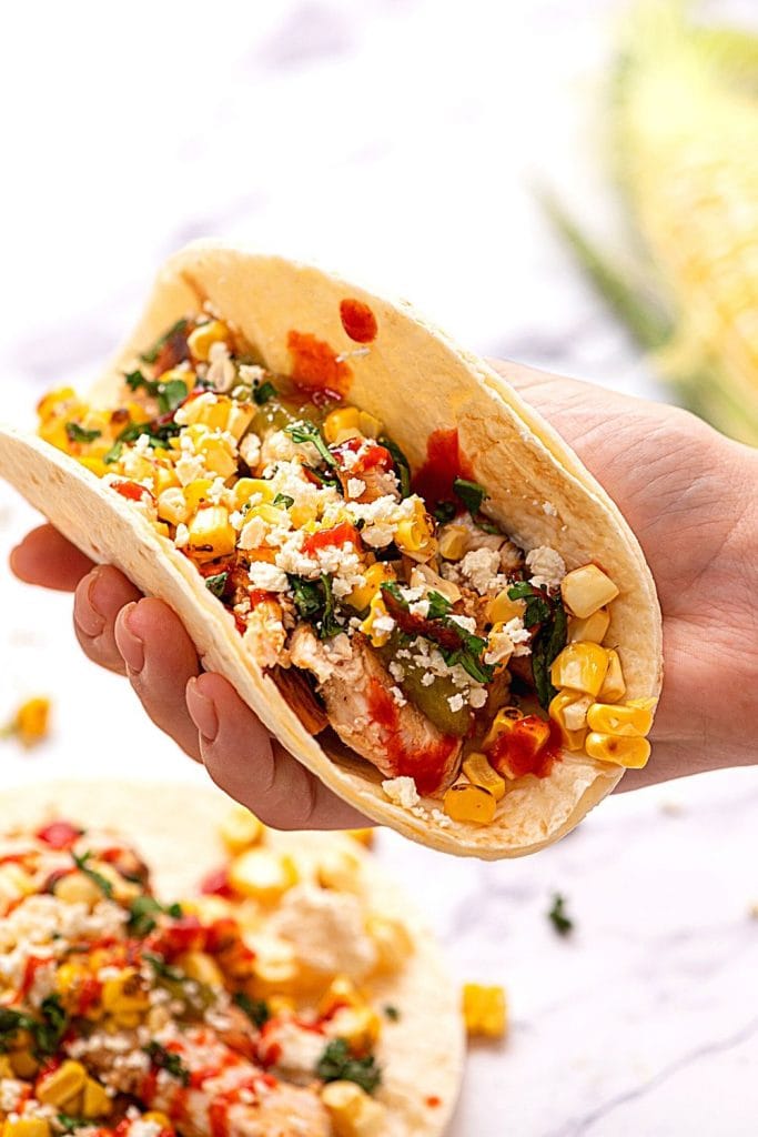 Hand holding grilled chicken fajita topped with corn salsa.