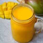 Bright Orange Mango Smoothie in glass jar next to fresh mango and ginger