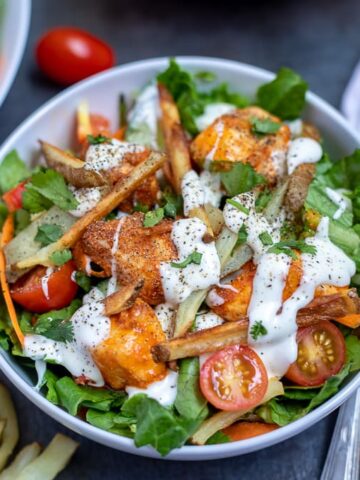 Bowl with salad topped with buffalo chicken, ranch and fries