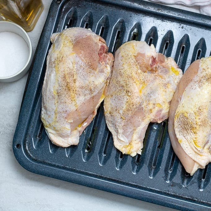 Raw split chicken breast on baking sheet with salt and pepper.