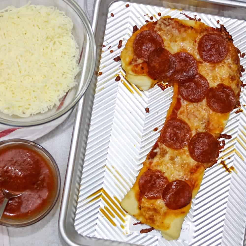 Candy Cane Shaped Pizza on baking sheet next to shredded cheese