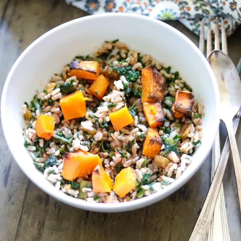 Brown rice, roasted butternut squash are tossed together with kale in white bowl