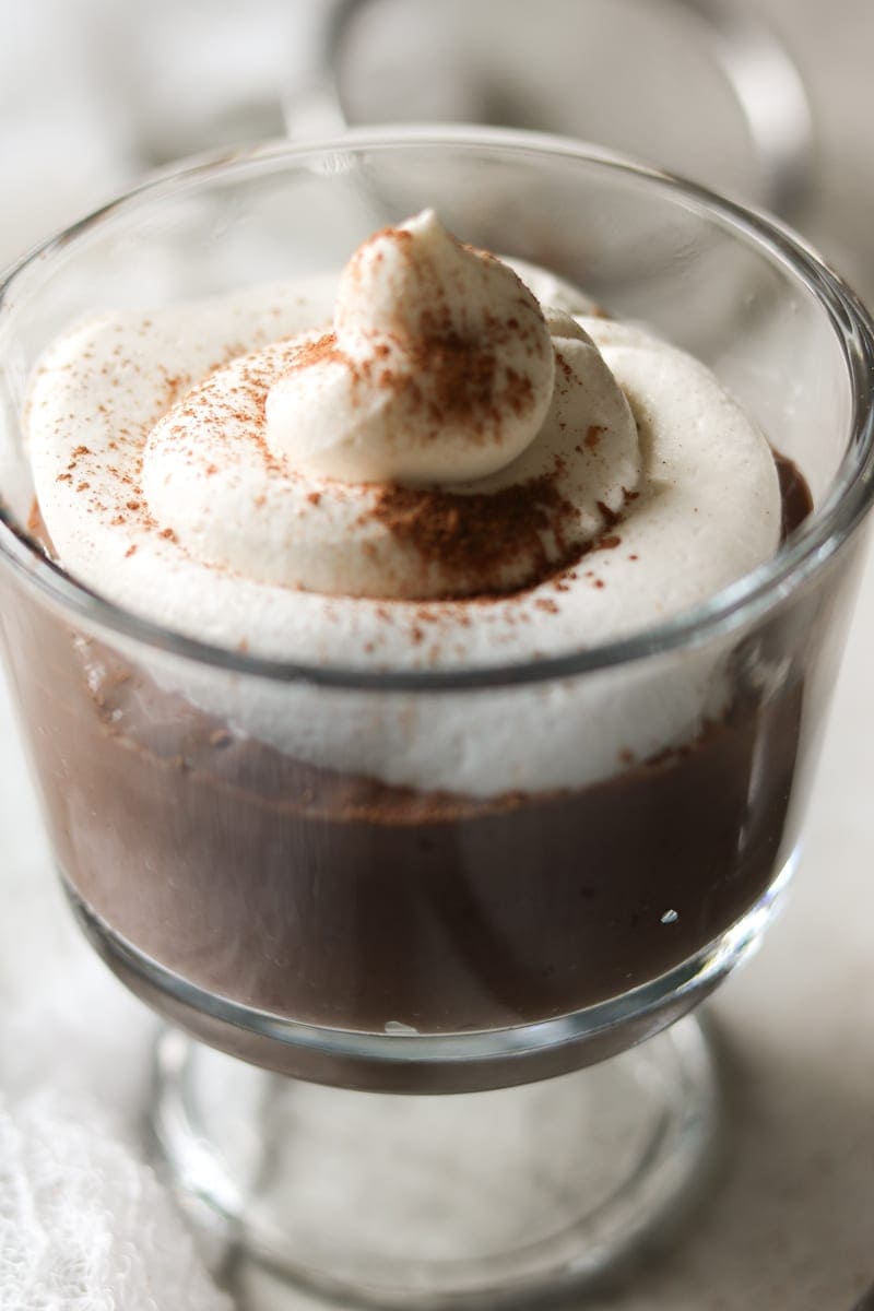 A velvety smooth rich chocolate mousse in a glass serving dish topped with a swirl of whipped cream dusted with cocoa powder. 