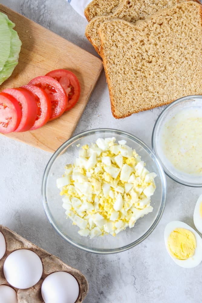 Chopped Hard Boiled Eggs in clear Bowl next to ingredients for egg salad. 