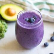 Clear class of Blueberry Smoothie with Kale and Avocados surrounding glass