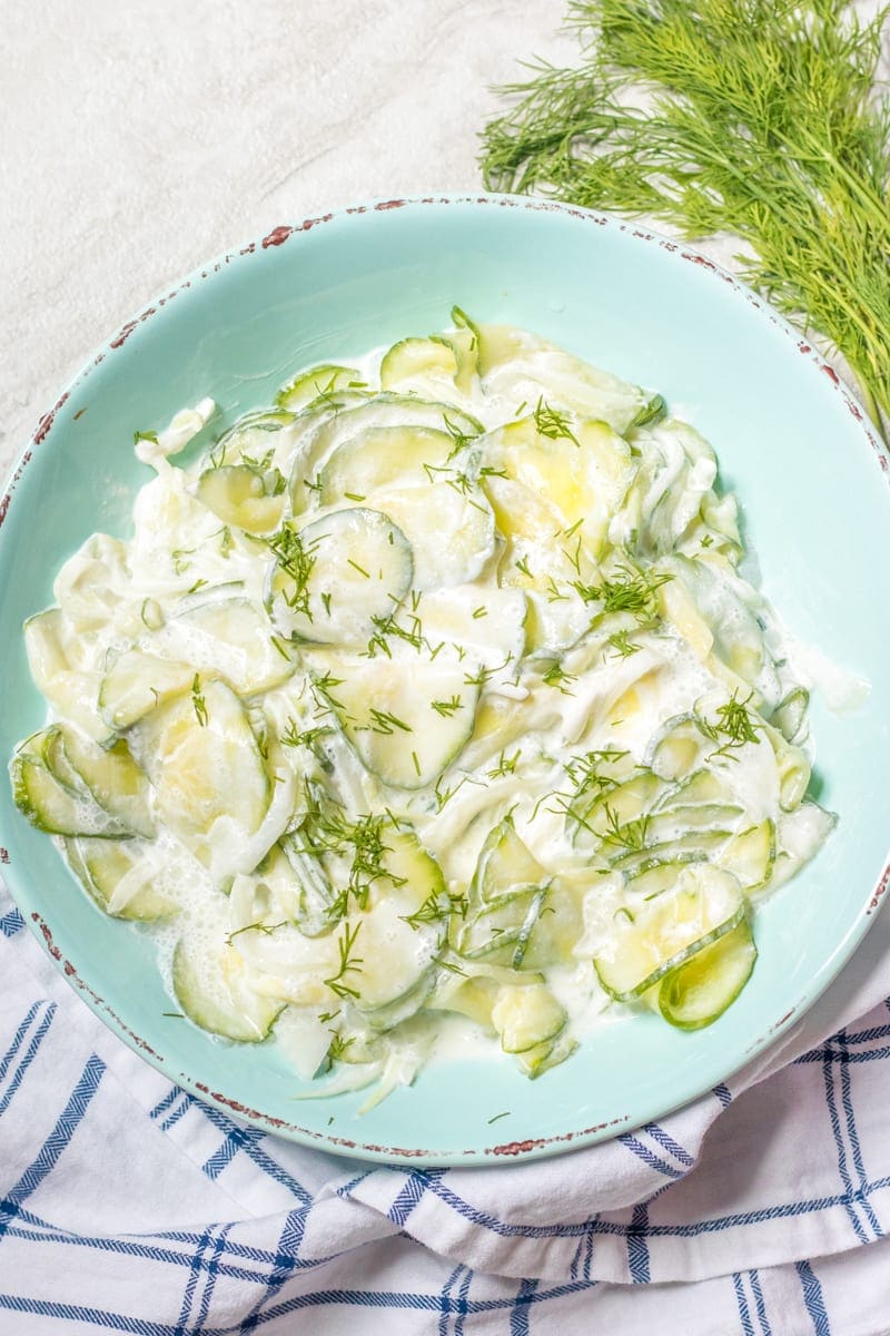 Bowl of creamy sour cream cucumber salad with fresh dill in blue serving dish. 