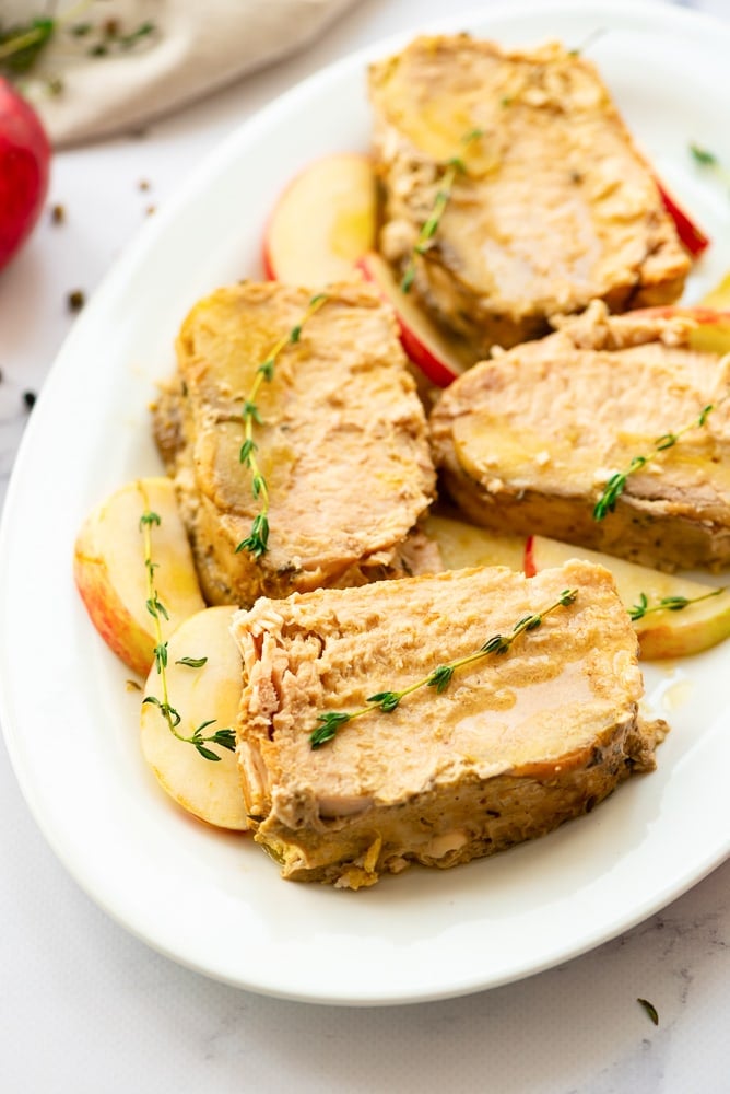 Sliced pork roast on white platter with apples and thyme