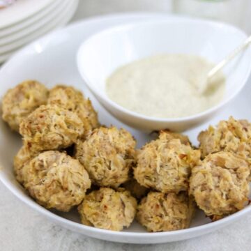 Baked sauerkraut balls in white dish with mustard sauce to the side