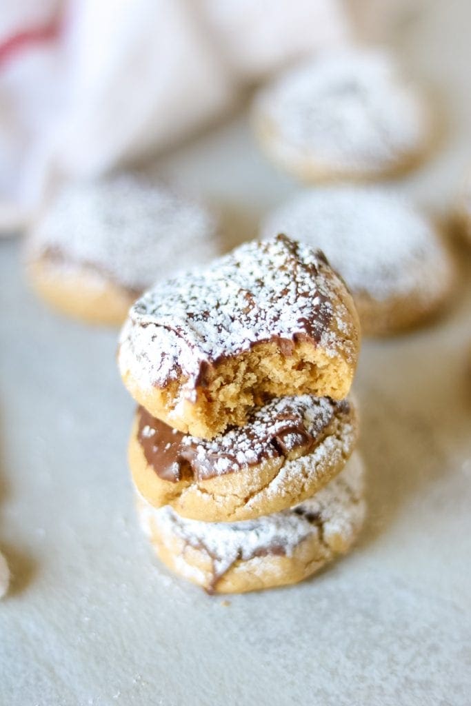 Stack of 3 Chocolate Dipped Peanut Butter Cookies dusted with powdered sugar with addtional baked cookies in the background. 