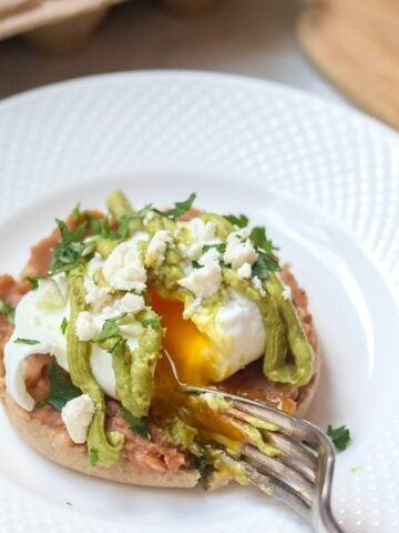 A perfectly poached egg sits upon a spicy refried beans on a toasted muffin and a creamy Avocado Hollandaise. 
