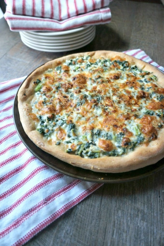 Pizza topped with ricotta, white sauce and spinach. 