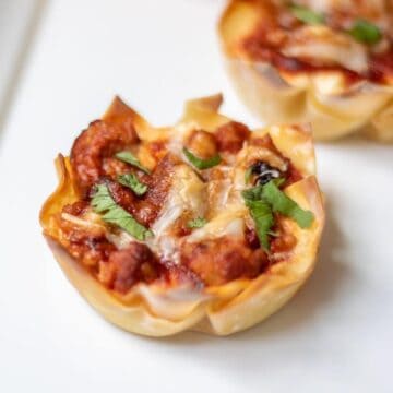 Mini Lasagnas made with wonton wrappers topped with fresh basil on white platter
