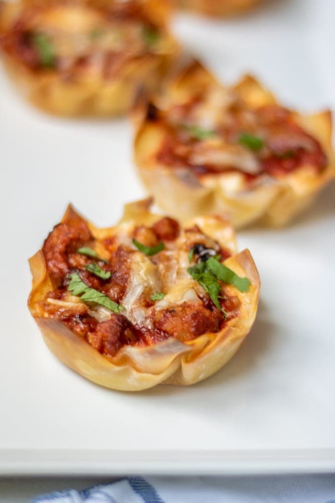 Mini Lasagnas made with wonton wrappers topped with fresh basil on white platter