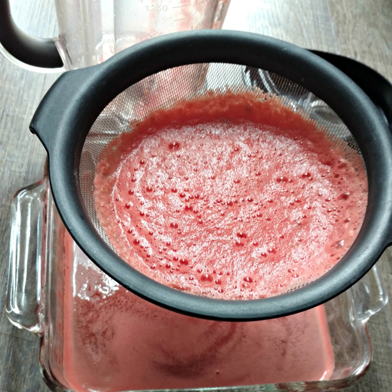 Fine Mesh Strainer with watermelon juice over glass baking dish.
