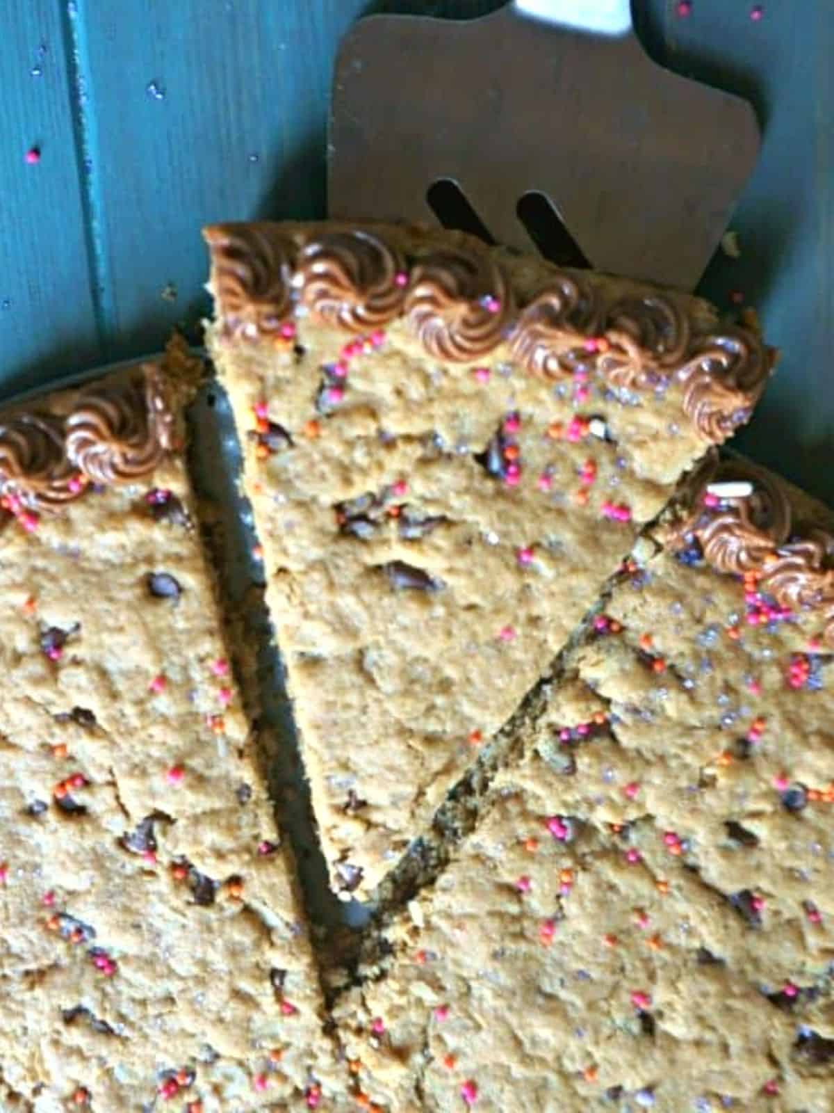 Slice of gluten free cookie cake with chocolate piping and sprinkles.