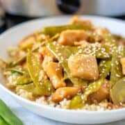 Mongolian Chicken in white bowl with snow peas and sesame seeds