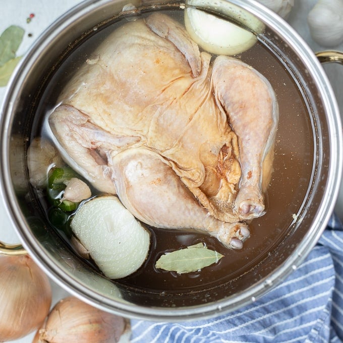 Raw chicken in large stock pan with onions, garlic and bay leaves
