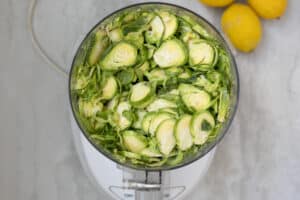 Shaved Brussels Sprouts in food processor next to fresh lemons