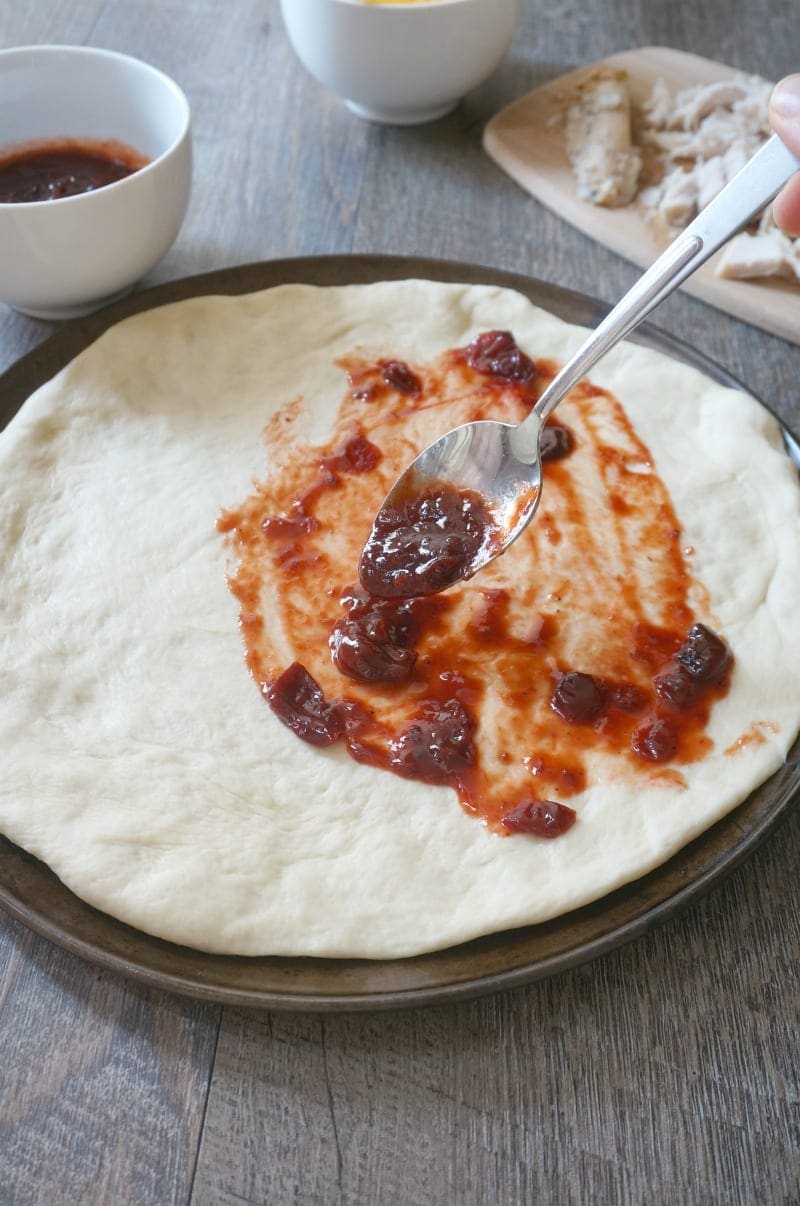 Cranberry BBQ Sauce being spread over pizza crust.