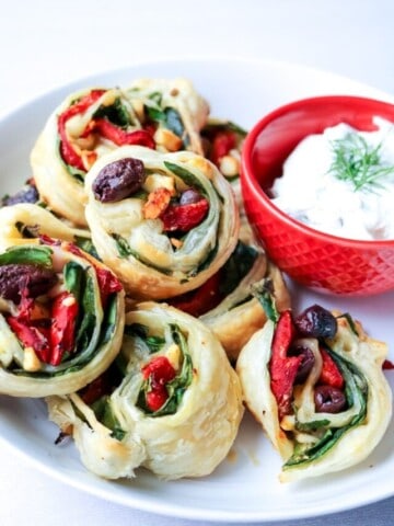 Simple Greek Pinwheels with Tzatziki Dipping Sauce: Spinach, roasted red peppers, olives, and feta are rolled up in buttery puff pastry and then served up with a Dill Tzatziki sauce.
