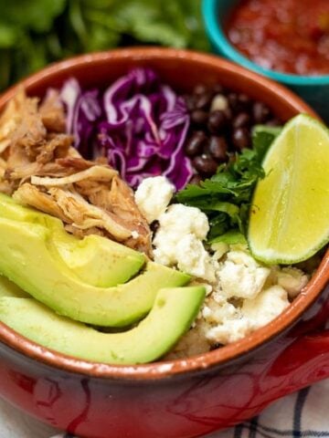 Red bowl with rice, shredded pork, avocado, cabbage and cheese