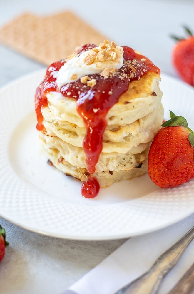 Stack of Strawberry Pancakes on White Plate topped with fresh strawberry sauce.