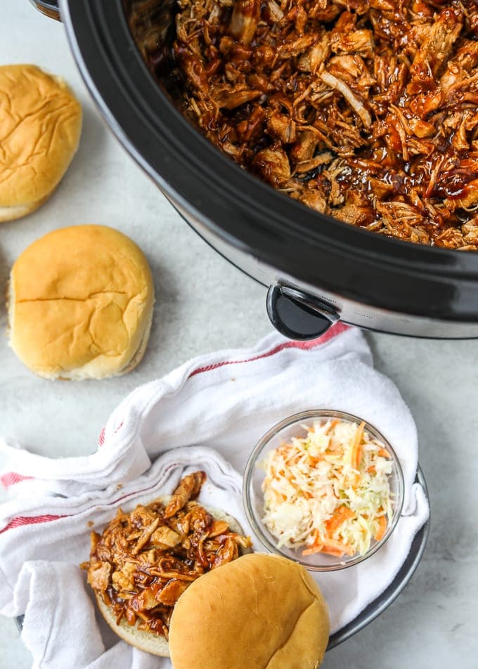 Slow Cooker filled with BBQ Pulled Pork next to buns.