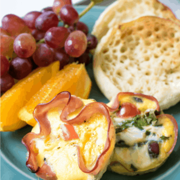 Eggs baked into slices of ham on blue plate with fruit and english muffin