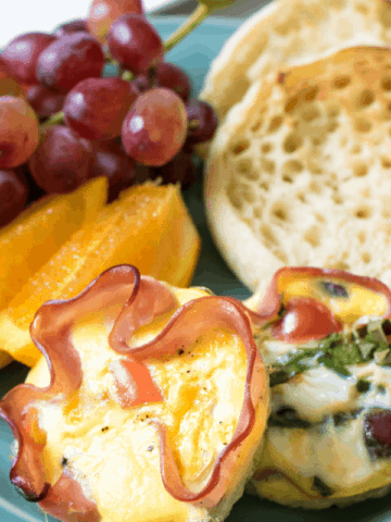 Eggs baked into slices of ham on blue plate with fruit and english muffin
