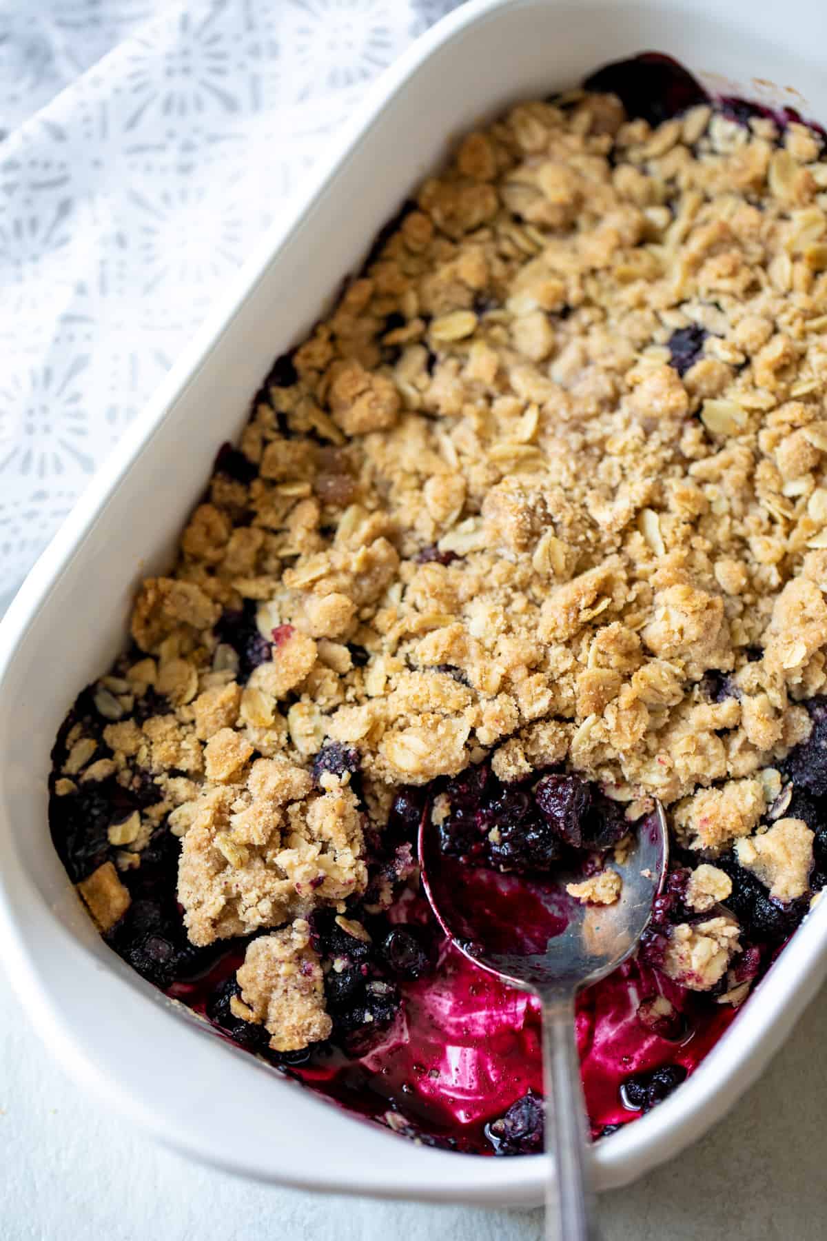 Baked Berry Crisp in white dish with spoon scooping out serving.