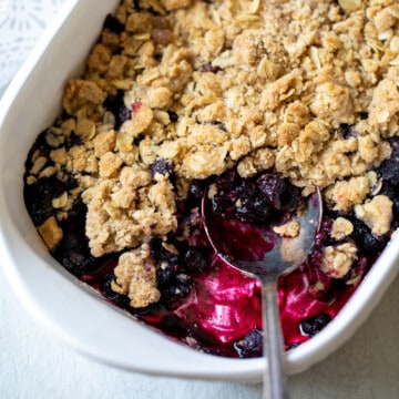 Baked Berry Crisp in white dish with spoon scooping out serving.