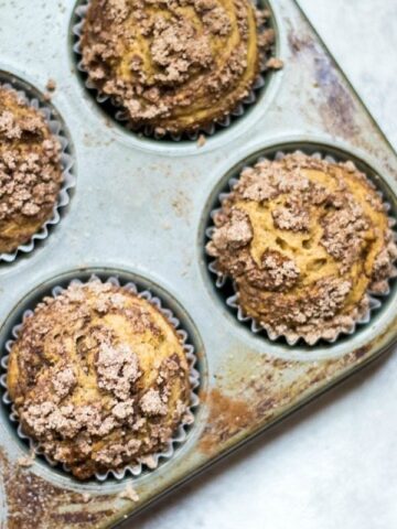 Picture of Gluten Free Cinnamon Streusel Muffins in silver muffin tin with cinnamon and topped with a delcioius Cinnamon Streusel. These muffins are gluten-free, dairy free and as delicious as any muffin you have ever had!