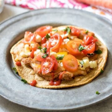 Southwestern Veggie Tostadas on silver plate topped with tomatoes and and corn