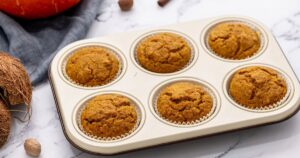 Baked Pumpkin Muffins in 6 cup muffin tin with nutmeg and coconut off to side