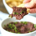 Black Bean dip with chip dipping into white bowl with title text overlay