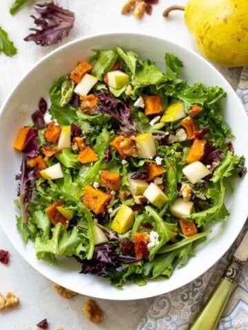 Greens topped with roasted butternut squash and cranberries in white bowl