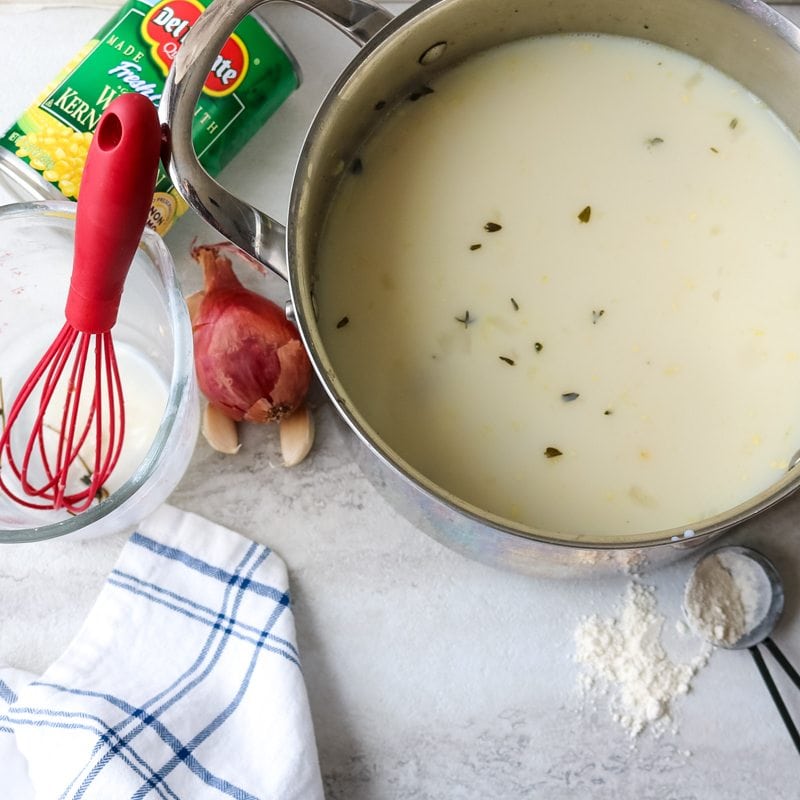 Corn and potato chowder in stock pan with red whisk whisking in cream and flour mixture
