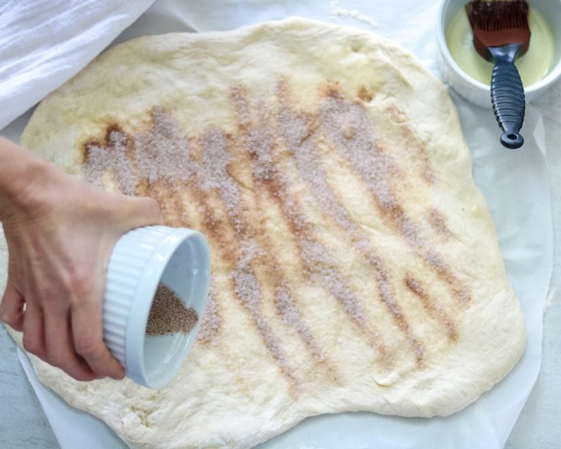 Sprinkling cinnamon sugar mixture over bread dough for cinnamon rolls.