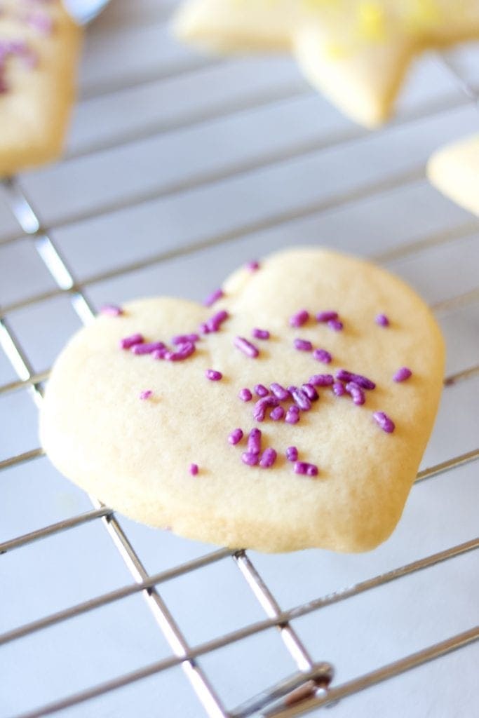 Cut out sugar cookie heart with purple sprinkles on cooking rack. 