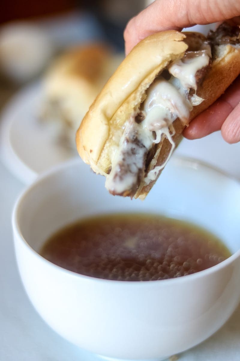 Cheesy French Dip Sandwich on Garlic Toasted Bun is being dipped into rich aus jus. 