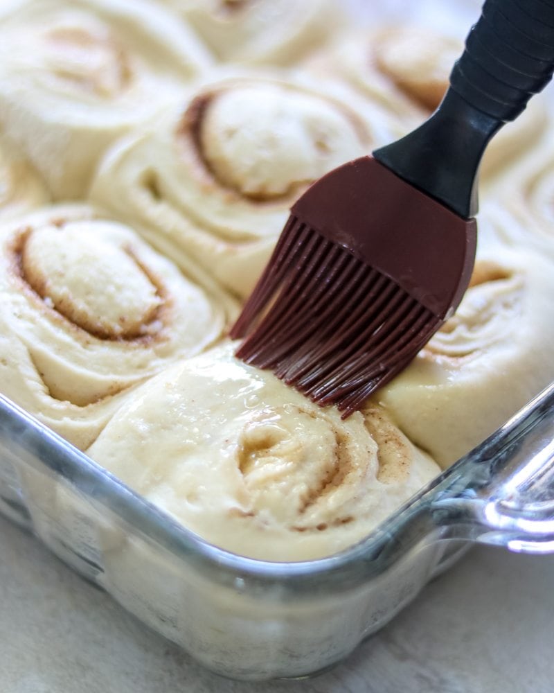 Pastry brush brushing melted butter on cinnamon roll dough