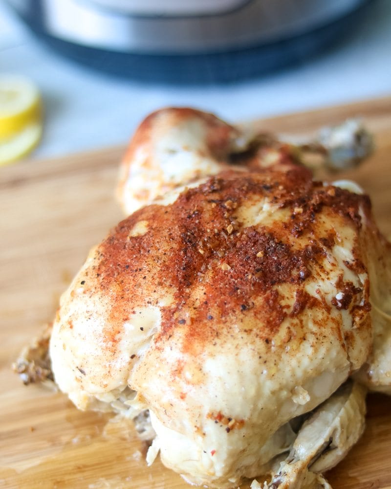 Rotissiere Chicken made in Instant Pot sitting on cutting board with pressure cooker in background.