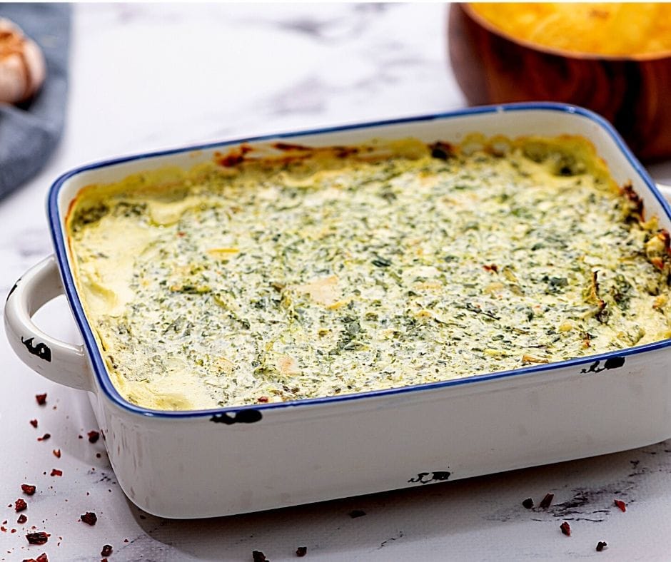 White Baking Dish filled with spinach dip served with tortilla chips on the side.