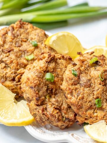 Baked Tuna cakes on white plate with green onions and lemon wedges