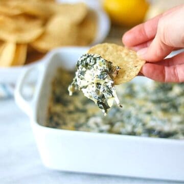 Tortilla Chip being dipped into baked spinach artichoke dip