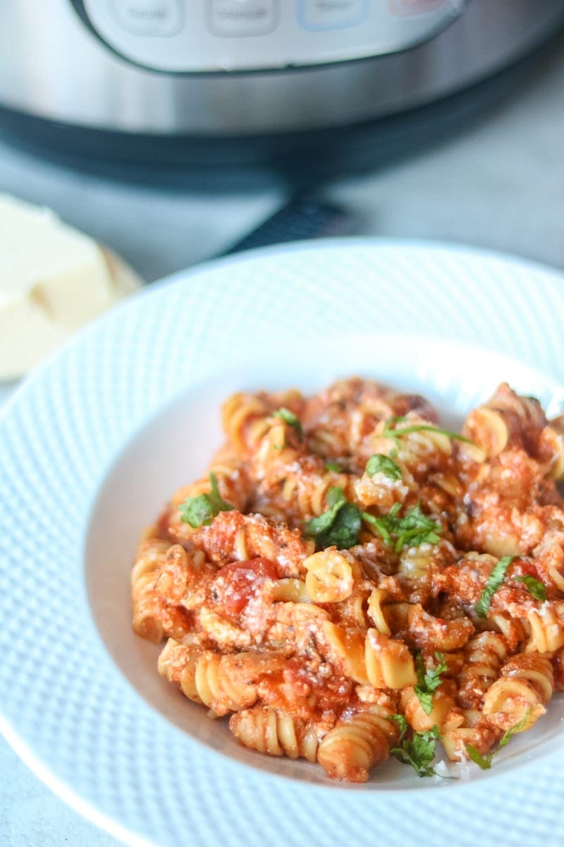 Instant pot in background with white bowl with rotini noodles with tomato sauce